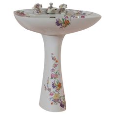 a white pedestal sink with colorful flowers painted on the side and faucet holes