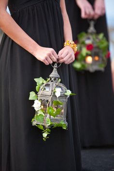 two women in black dresses holding small lanterns with flowers on them, and one is holding a