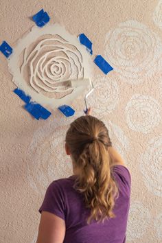 a woman is painting a wall with blue tape and some white circles on the wall