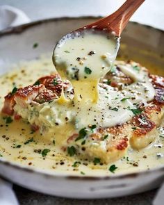 a wooden spoon scooping some food out of a white bowl with sauce on it