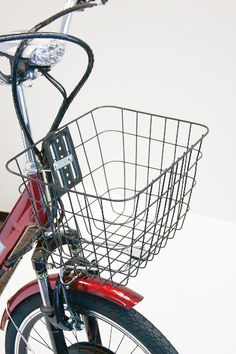 a red bicycle with a basket on the front and back tire, parked against a white wall