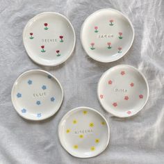 four small dishes with flowers painted on them sitting on a white cloth covered tablecloth