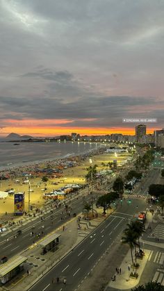 an aerial view of the beach and ocean at sunset, with cars parked on the road