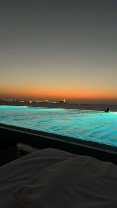 an empty swimming pool at night with the sun setting in the distance and buildings on the horizon