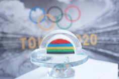 a glass object with a flag on top of it in front of the olympics logo