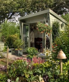 a garden shed with lots of plants and flowers in the front yard, next to a lamp post