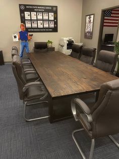 a man standing in front of a table with chairs around it and an american flag hanging on the wall