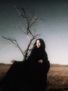 a woman standing next to a tree in a field