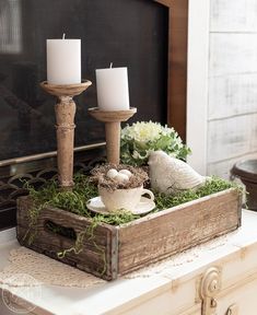 two candles are sitting on top of a box with moss and eggs in it, next to a bird figurine