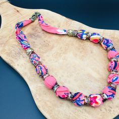 a pink and blue necklace sitting on top of a wooden board