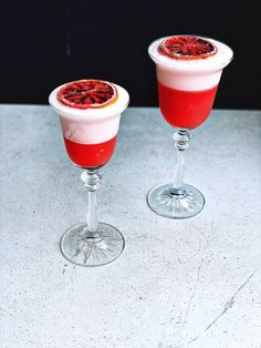 two glasses filled with drinks sitting on top of a white counter next to each other