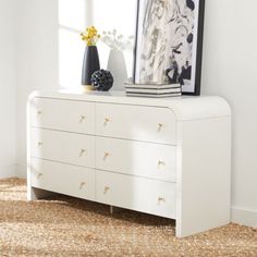 a white dresser with two vases on top of it and a framed photograph above it