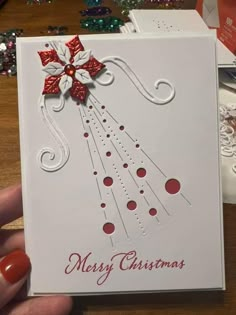 a hand holding up a christmas card with red and white decorations on it's side