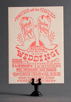 a red and white wedding card with two cowboy boots on it's legs, in front of a gray background