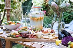 a wooden table topped with lots of food next to vases filled with flowers and vegetables