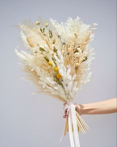 a bouquet of dried flowers being held by someone's hand on a gray background