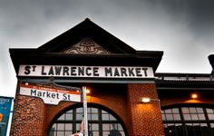 a street sign in front of a brick building with arched windows and dark clouds overhead