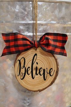 a wooden ornament that says believe hanging from a string with a red and black bow