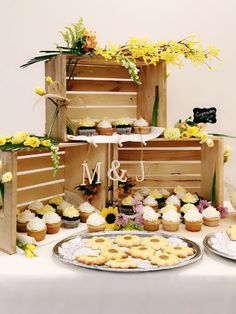 a table topped with lots of cupcakes next to wooden crates filled with flowers