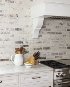 a kitchen counter with utensils on it in front of a brick wall and stove