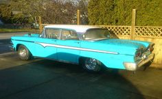 an old blue and white car parked in front of a wooden fence