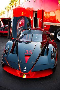 a red and black sports car parked in front of a truck