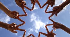 several hands making a star shape with their fingers in the air against a blue sky