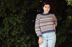 a woman standing in front of some trees wearing glasses and a sweater with stripes on it