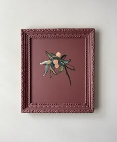 a red frame with some flowers on it hanging on the wall next to a white wall