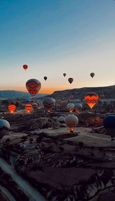 many hot air balloons are flying in the sky at sunset or dawn over an arid area