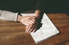 two people holding hands over a paper on top of a wooden table next to a pen