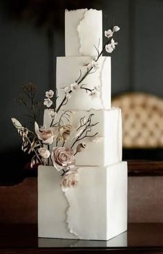 a three - tiered white cake with flowers on the top and side, sitting on a table in front of a chair