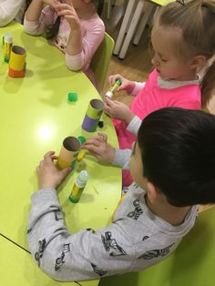 several children sitting at a table playing with cups and paper tubes on the table in front of them