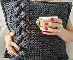 a woman holding a coffee cup while sitting on a couch with a knitted pillow