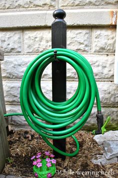 a green garden hose is attached to a black pole in front of a brick wall