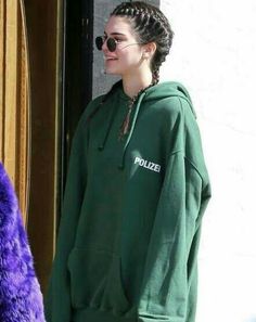 a woman with braids wearing a green hoodie and black sunglasses standing in front of a door