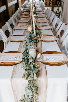 the long table is set with white linens and greenery