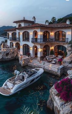 a boat that is sitting in the water next to a large house with lights on it