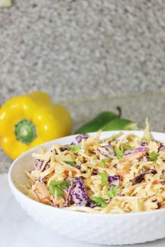 a white bowl filled with coleslaw slaw next to yellow peppers and pepper