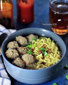 a bowl filled with meatballs and noodles on top of a blue table cloth next to two jars