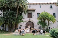 an outdoor wedding ceremony in front of a large white building with palm trees and chairs