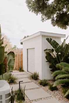 a small white shed sitting next to a lush green tree