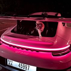 a cat sitting in the trunk of a pink sports car with its headlight on