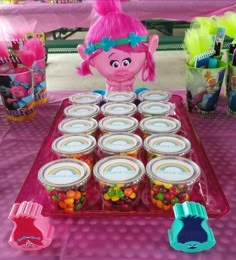 there is a table with many candy jars and cupcakes in the shape of a troll