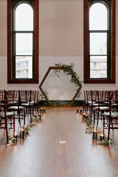 an empty room with rows of chairs, candles and greenery on the floor in front of two large windows