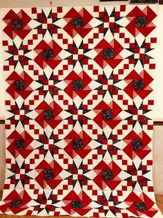 a large red and white quilt with black squares on the front, sitting on top of a wooden floor