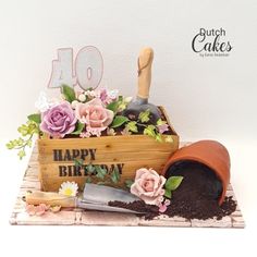 a birthday cake with flowers in a wooden box and gardening utensils on top