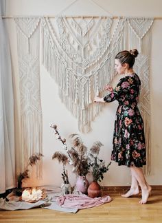 a woman standing in front of a wall hanging with tassels and flowers on it