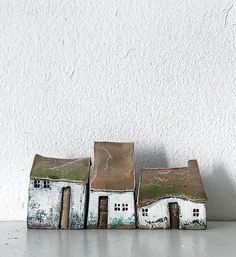 three small white houses sitting next to each other on top of a table in front of a white wall