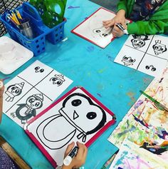 two children sitting at a table painting pictures on paper with crayons and markers